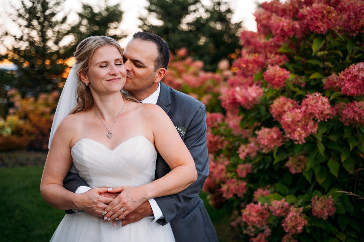 groom kissing brides cheek in front of flowers