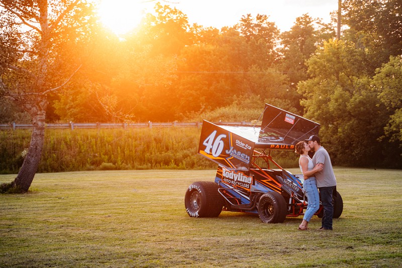 couple kissing at sunset with race car in background