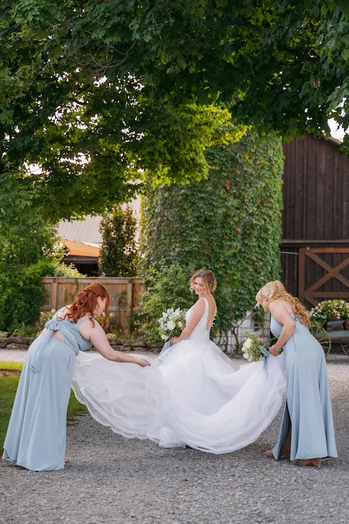 Bridesmaids helping with brides dress outside at Maple Meadows Farm