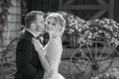 Groom kissing bride on her cheek during portraits at Maple Meadows Farm wedding