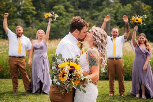 bride and groom kissing with wedding party in background