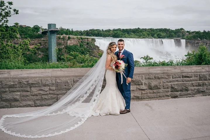 bride and groom standing infront of niagara falls