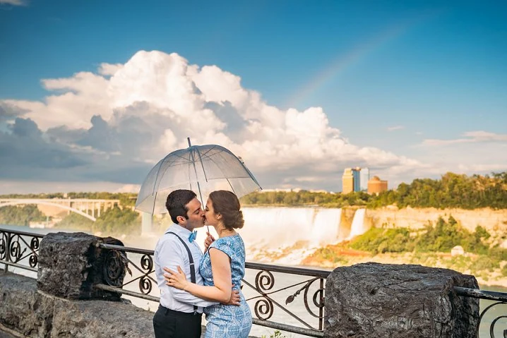 bride and groom kissing in front of niagara falls with a rainbow behind them